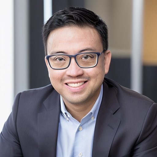 A man in glasses and suit jacket smiling.