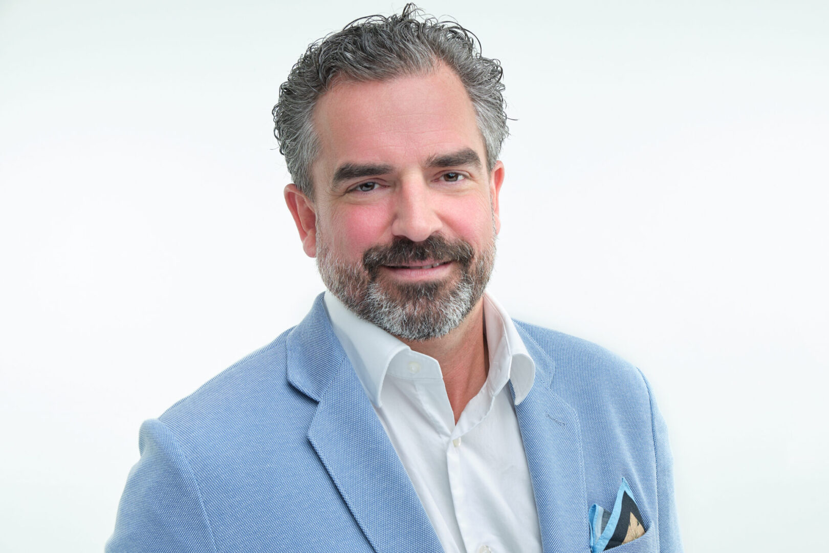 A man with grey hair and beard wearing a blue suit.